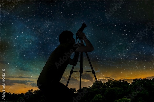 Silhouette of photographer is taking photos of stars and night sky with camera on tripod.