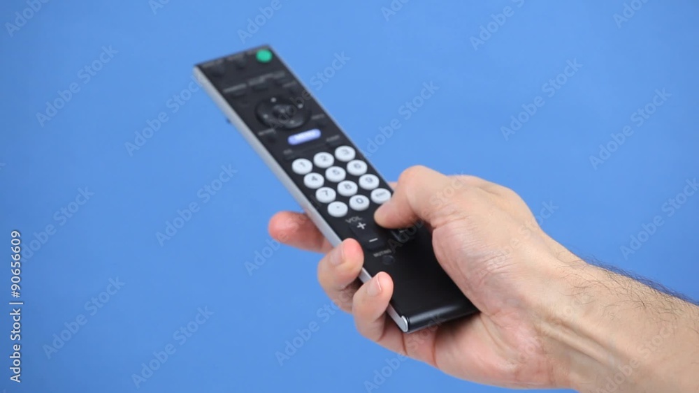 Close up of a remote control in hand on blue background Close up of a remote control in hand on blue background