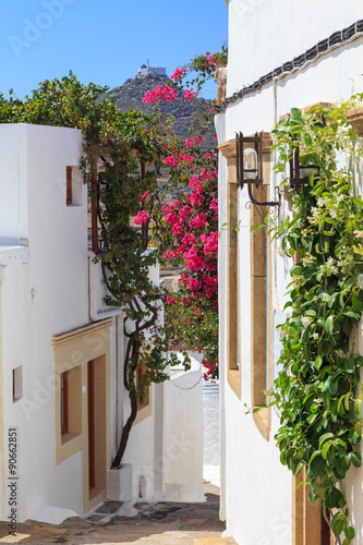 Narrow street in Chora on the island of Patmos, belonging to the Dodecanese, Greece. Beautiful flowers of bougainvillea contrast to the white walls of houses and blue sky © stepmar