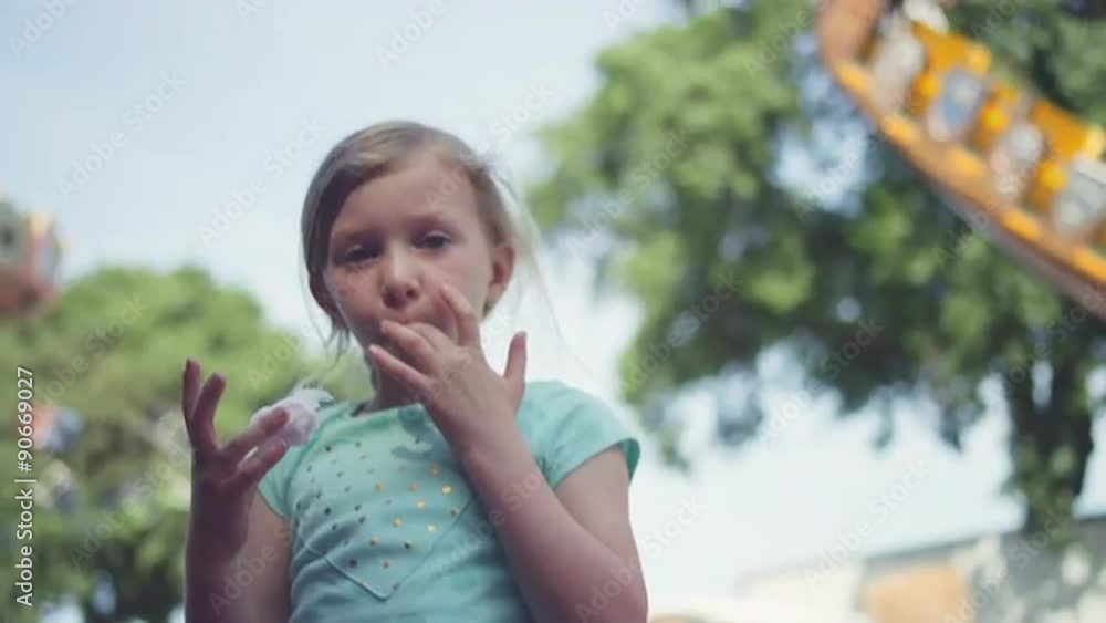 A young girl eating cotton candy with carnival rides in the background
A young girl eating cotton candy with carnival rides in the background