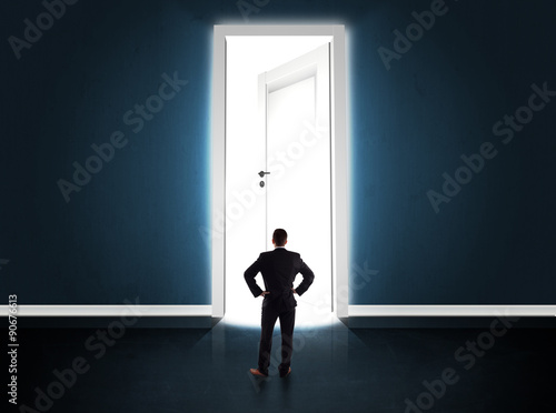 Business man looking at big bright opened door