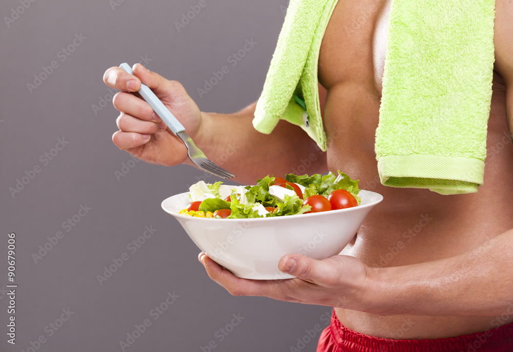 Fit man holding a bowl of fresh salad on grey background Fit man holding a bowl of fresh salad on grey background