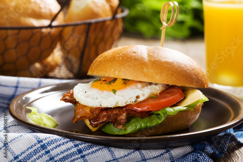 Sandwich with a fried egg, bacon, cheese and vegetables.