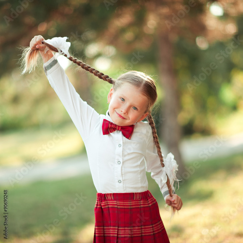 Kid girl having outdoors. Smiling child. Looking at camera. Wearing stylish school uniform. Back to school.  photo