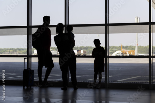 silhouette family at airport in front of window watching airplanes take off and land
