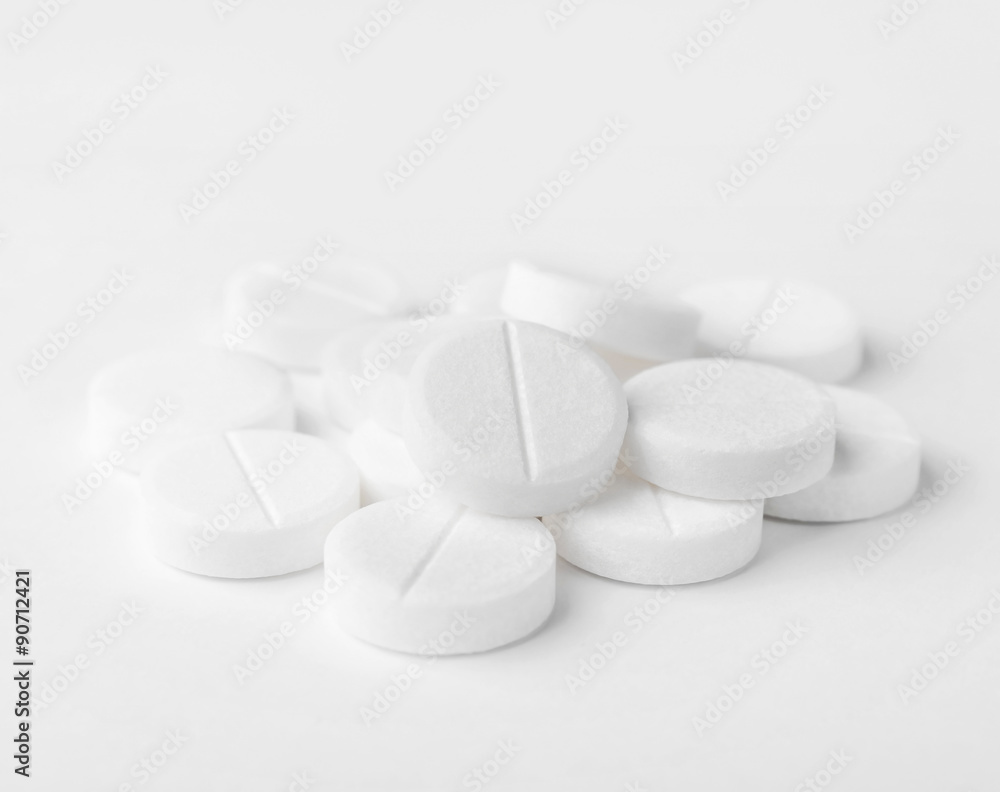 A heap of white medicine pills on white surface.