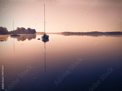 Little sailing boats reflect in the serene water during sunrise.
