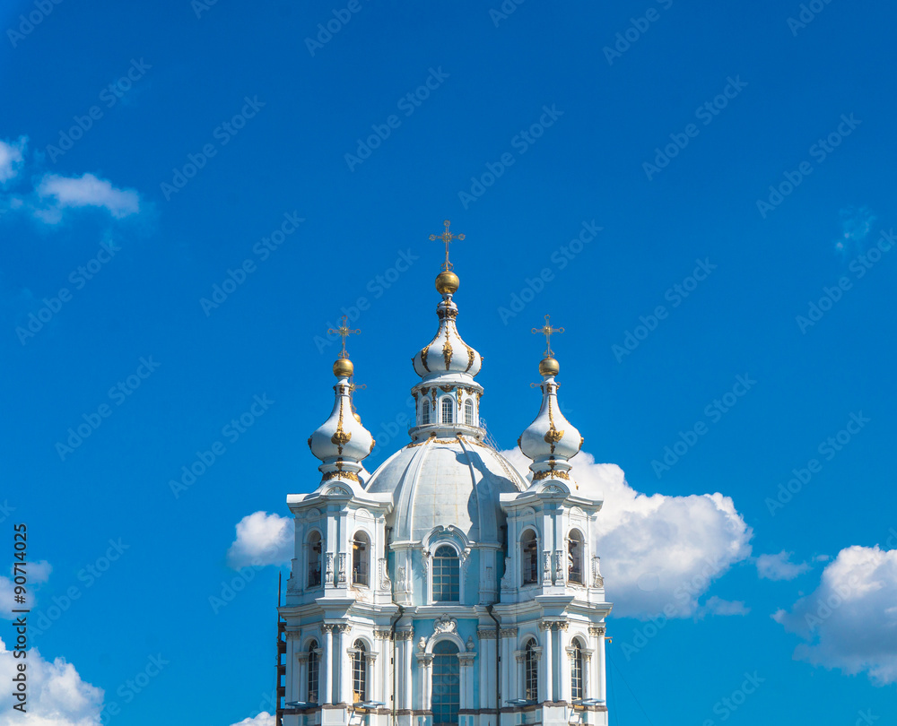 The powder blue and white domes of Smolny Cathedral against the bright blue sky with a few white clouds 