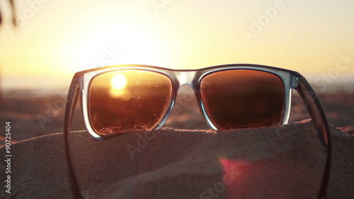 steady shot of sunset on sandy beach through sunglasses with people silhouette