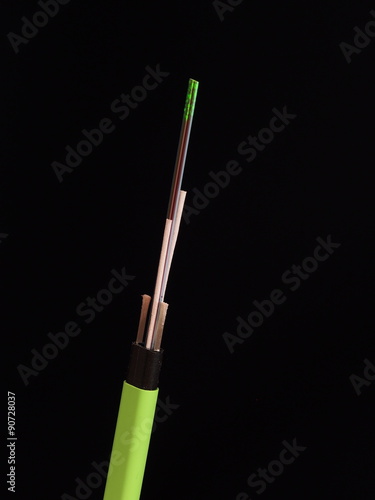 Green Nylon coated fiber optic cable with stripped and exposed fibers lit by green laser light in front of a black background, Melbourne 2015 