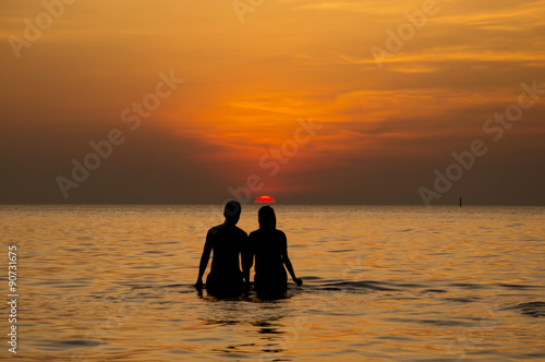 Silhouette of couple walking in to the sea at sunset