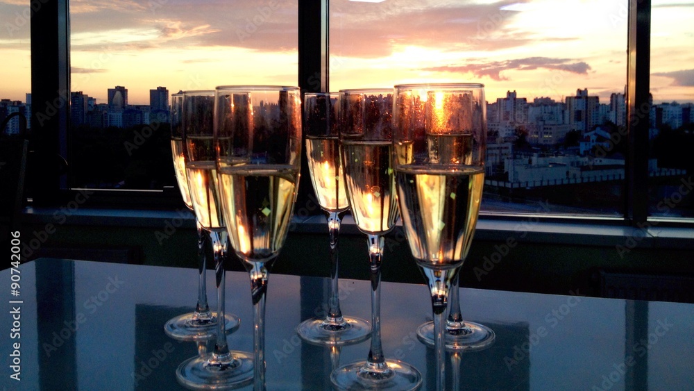 several sparkling wine glasses on a table top against window with sunset over city