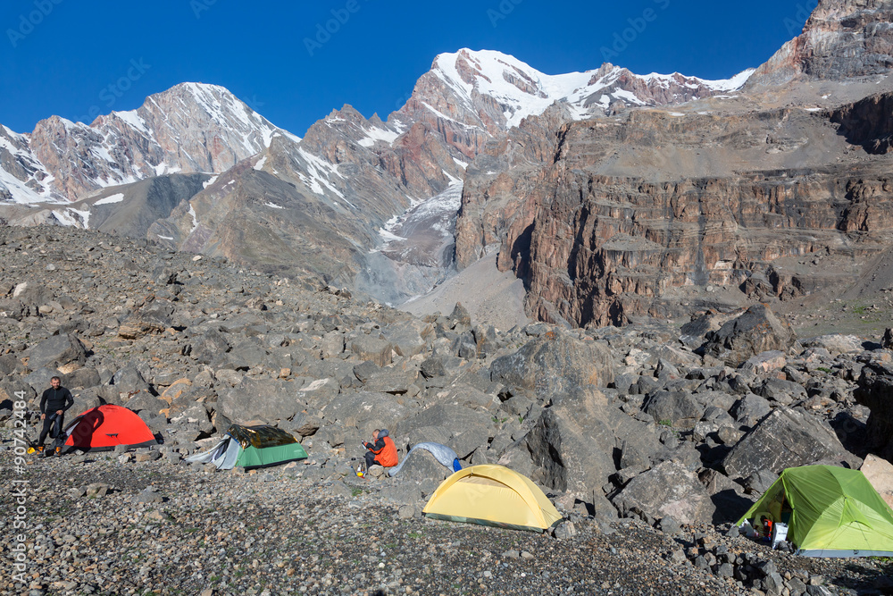 Mountain Expedition Camp in Morning Four tents Yellow Green Red Located on Rocky Moraine Mountain View on Background with Glaciers People Walking and Preparing to Ascent