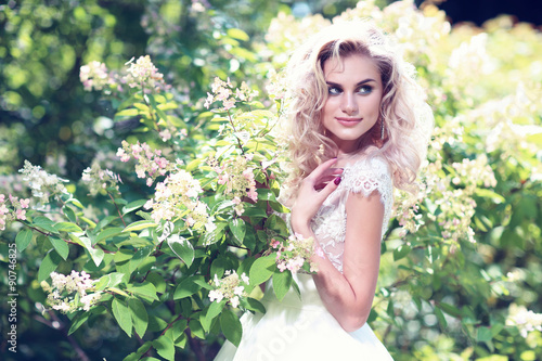Beautiful bride posing outdoor. Wedding dress, curly blond hair.
