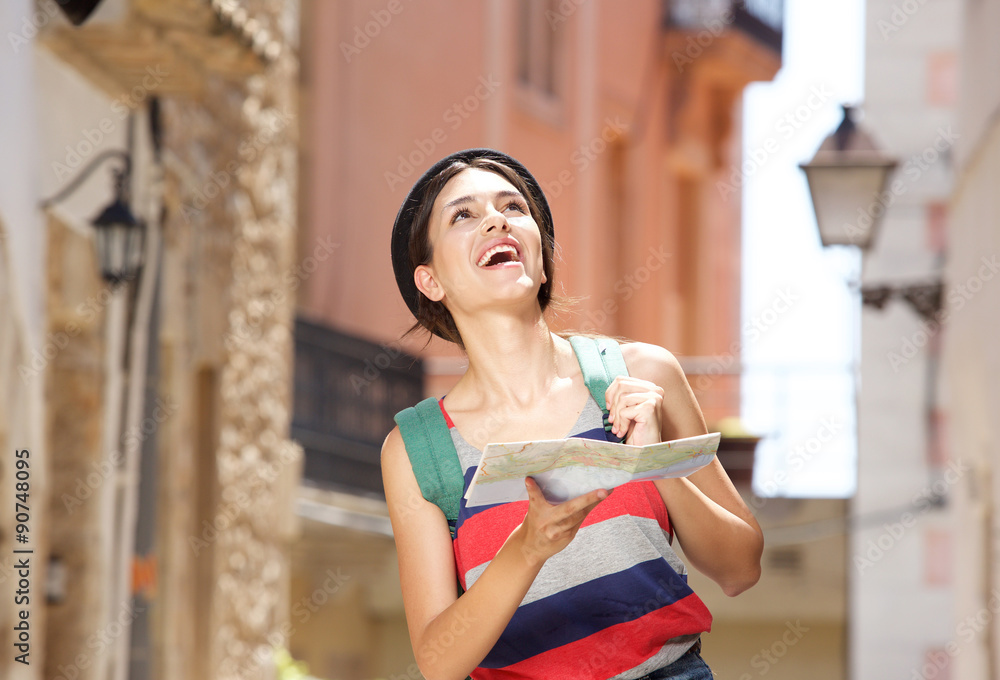 Cheerful young woman walking in town with bag and map
