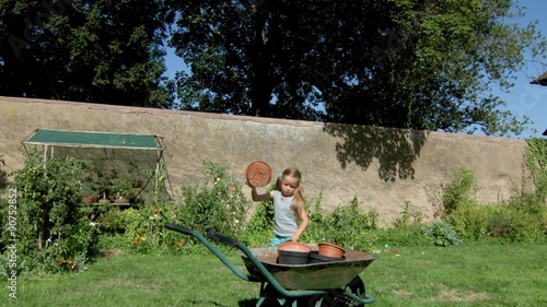 Cute little girl riding hand-barrow in the backyard, summer day photo