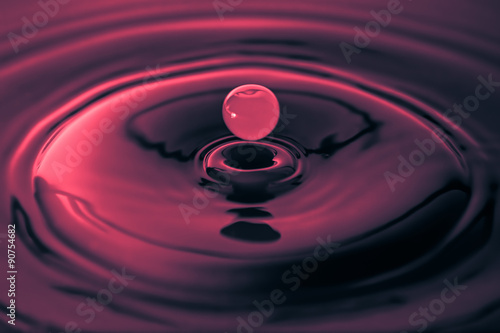 Water drop falling to a red liquid surface