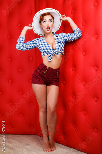 Sexy retro pin up girl with hat in hand, isolated on red