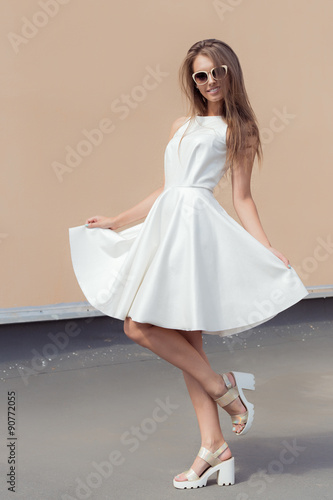 Pretty sweet beautiful girl in a bright white dress in fashionable shoes and sunglasses spinning on the roof