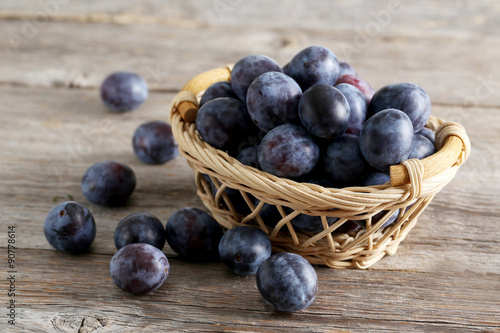 Fresh plums in basket on brown wooden background
