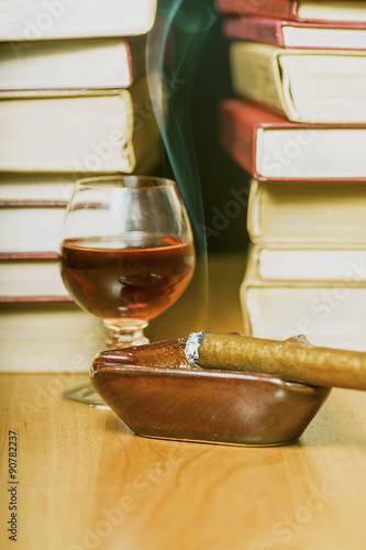 Zapalone cygaro z drinkiem na tle książek