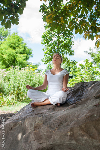 20s blond girl meditating under a tree on a stone