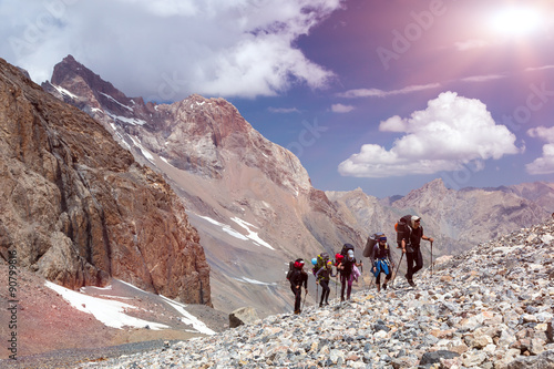 Group of Mountaineer Walking on Deserted Rocky Terrain Five Members Team Sport Clothing Going Heavy Load Backpacks Climbing Gear Up Mountain Peaks Blue Sky Majestic Summits Shining Sun Background