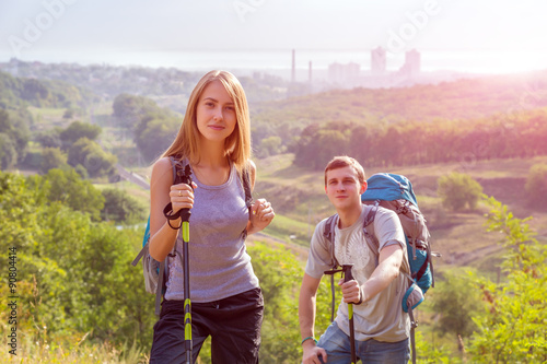Excited Hikers Young Man Woman Traveling Outdoor Expressing Fun and Pleasure with Backpacks Walking Poles Sticks and Casual Sporty Style Clothing Forest Suburban Park Landscape Sunrise Sun Background