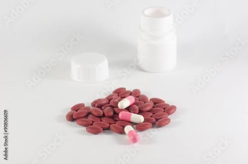 dark red and pink pills spilling from a white plastic bottle