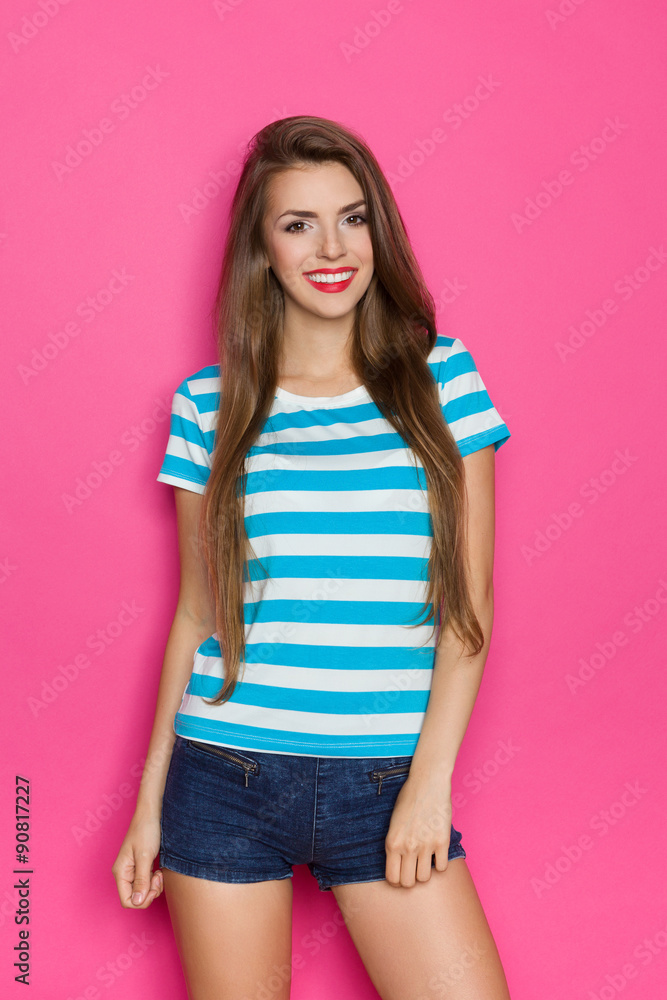 Beautiful young woman in stripped shirt and jeans shorts posing against pink wall. Beautiful young woman in stripped shirt and jeans shorts posing against pink wall.