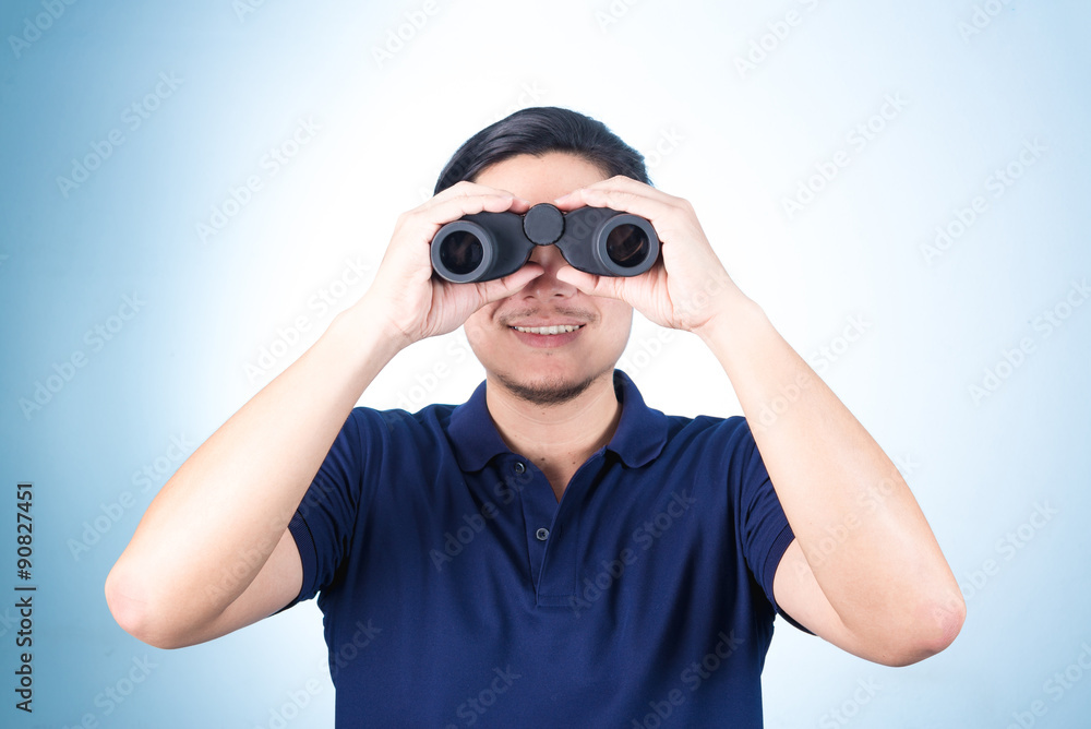 Asian guy holding binoculars, on blue background Asian guy holding binoculars, on blue background