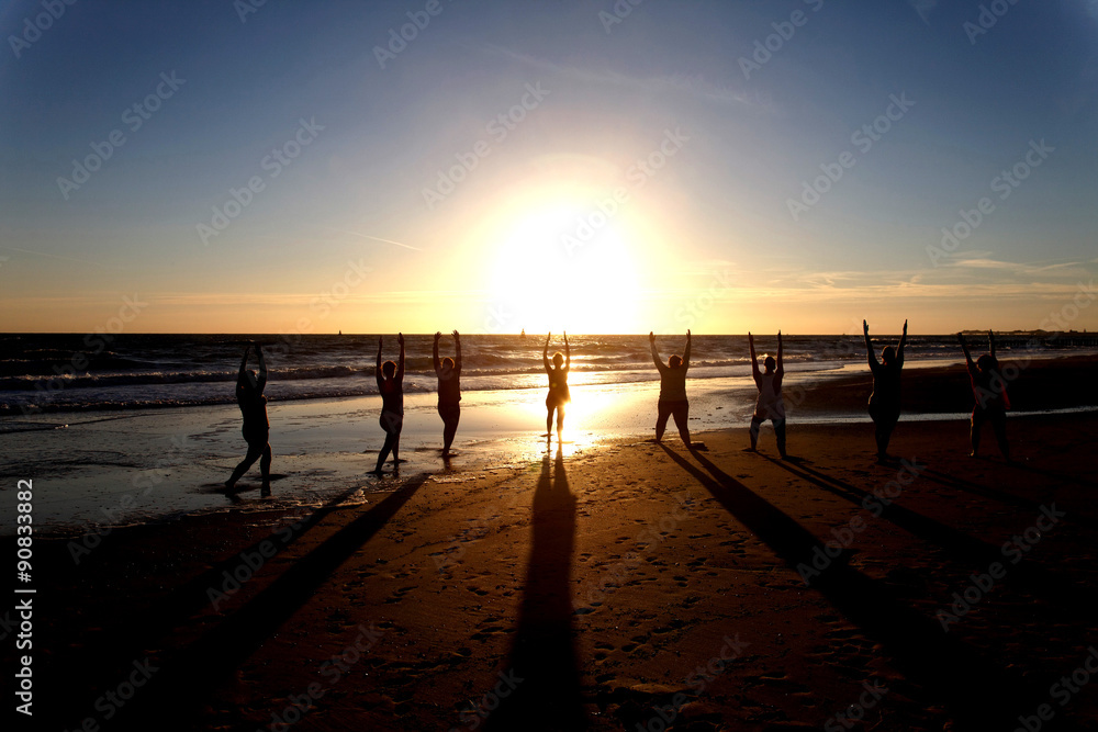 yoga in group as silhouette by the sea at sunset