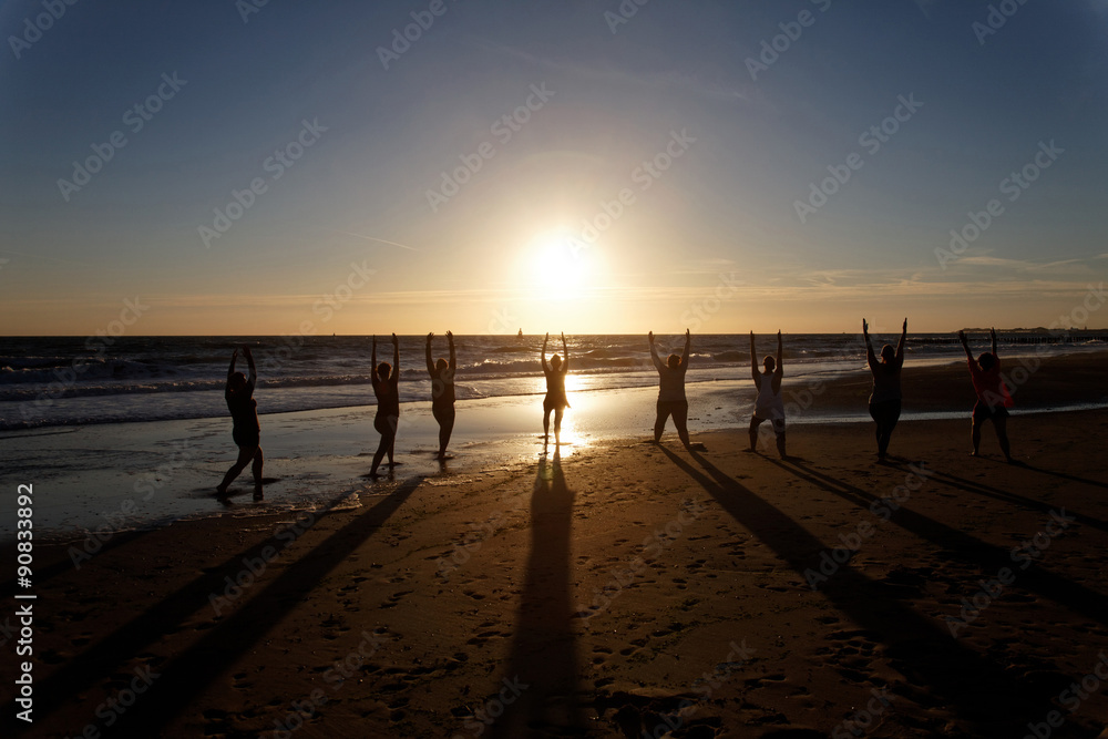 yoga in group as silhouette by the sea at sunset