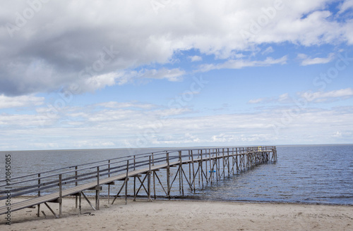 horizontal image of a long wooden pier jutting out over the ocean into the distance under a blue summer sun with clouds floating by with room for text. © nat2851terry