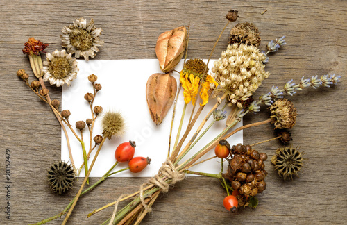Dried flowers and a white paper on the wooden background