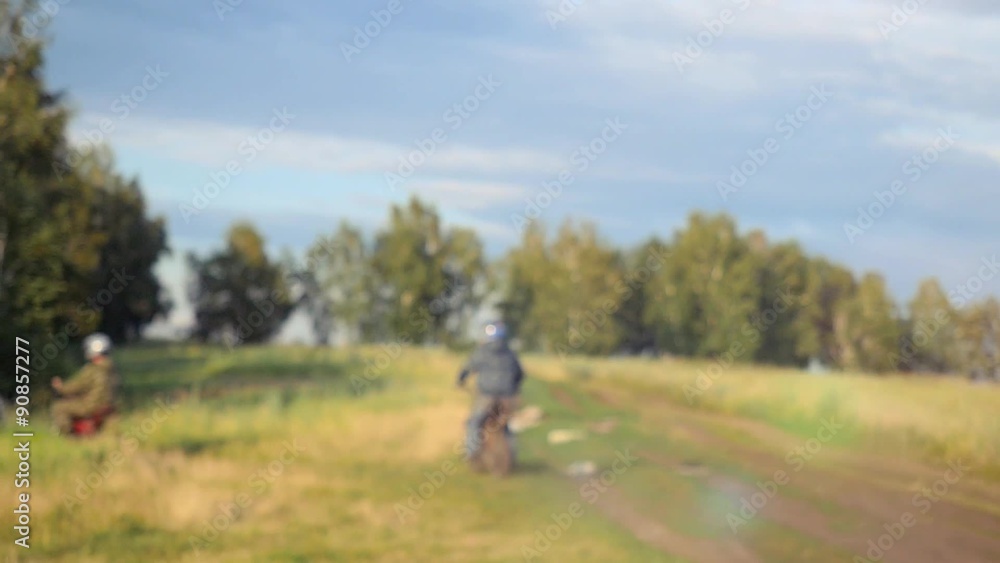 Two motorcyclists on bike going to the forest on road in field Two motorcyclists on bike going to the forest on road in field