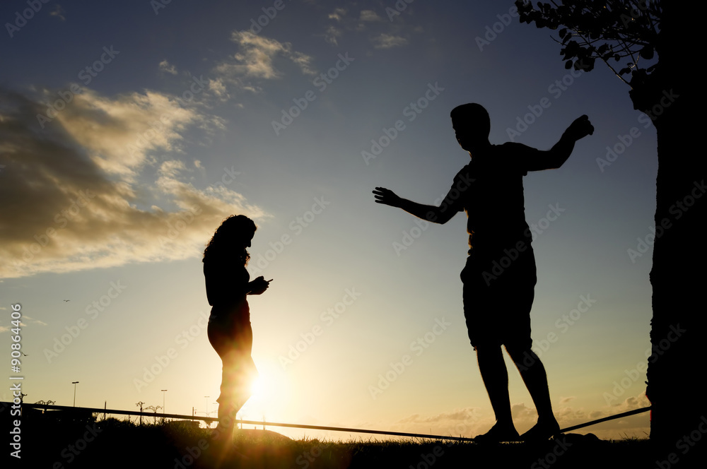 man balancing in slack line , slacklining , and woman looking  mobile