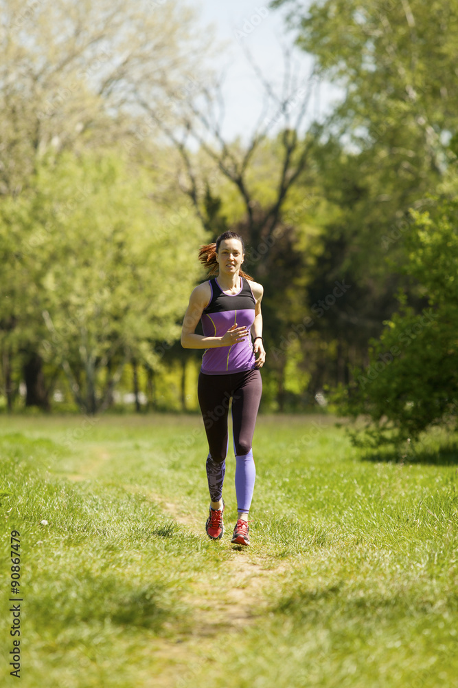 Jogging woman running in park in sunshine on beautiful summer day.