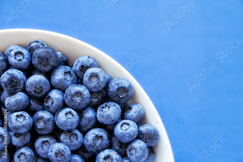 Blueberries in white bowl on colorful blue backround