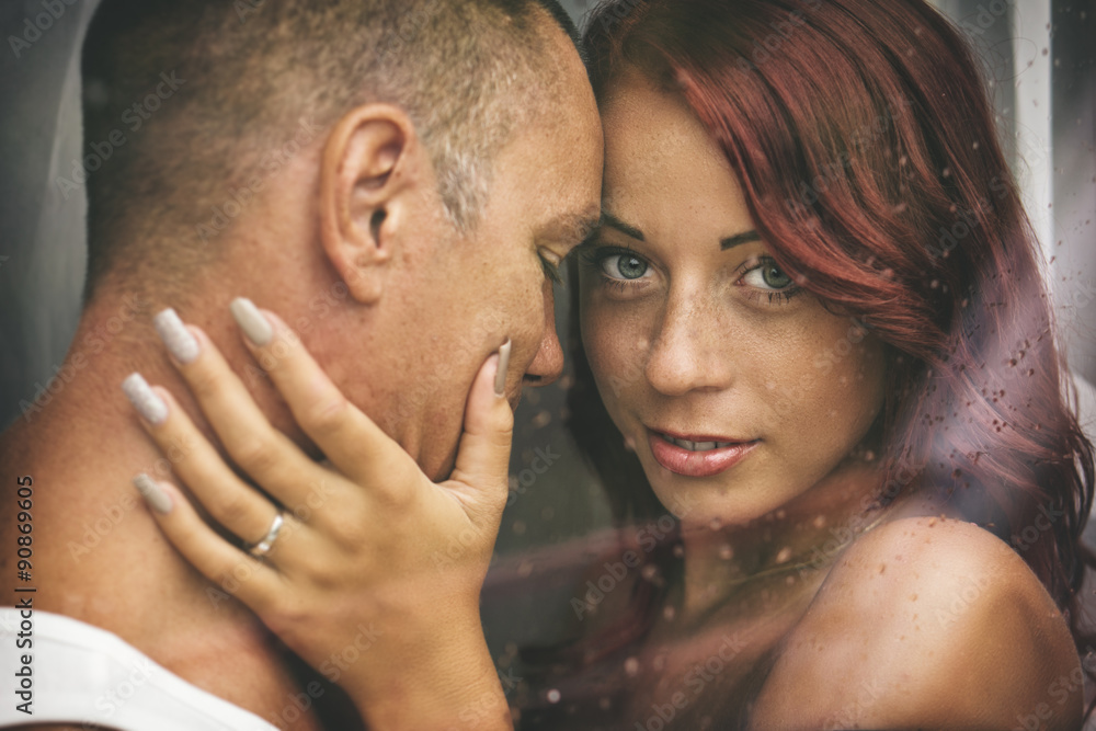 Fototapeta premium Attractive couple behind a window with water drops, in a rainy day.