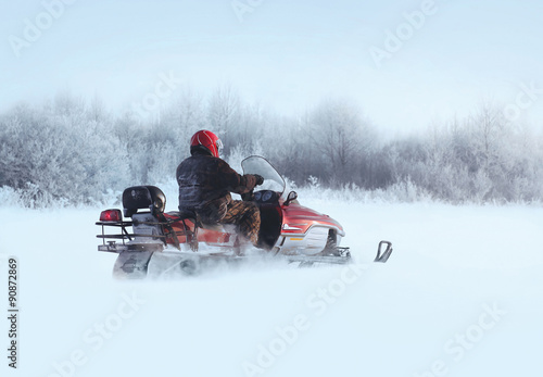 Man rides a snowmobile through the snowdrifts in winter day
