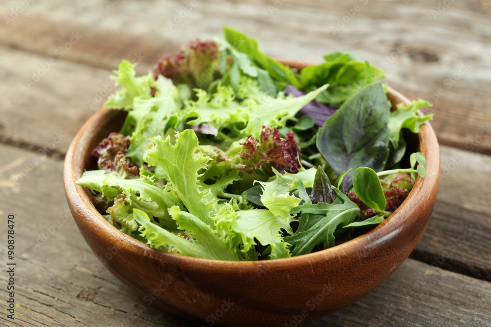 Fresh mixed green salad in bowl on wooden table close up Fresh mixed green salad in bowl on wooden table close up