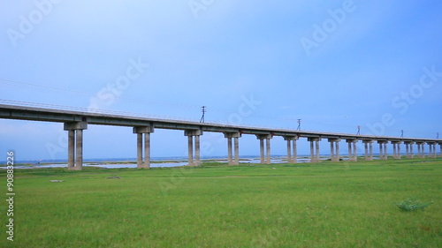 panning shot of Bridge of railway cross grass field meadow at Pasuk River Dam in summer, Lopburi, Thailand photo