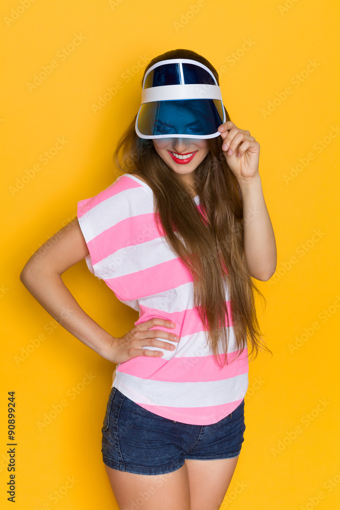Fototapeta premium Smiling Woman In Transparent Plastic Blue Sun Visor. Three quarter length studio shot on yellow background.