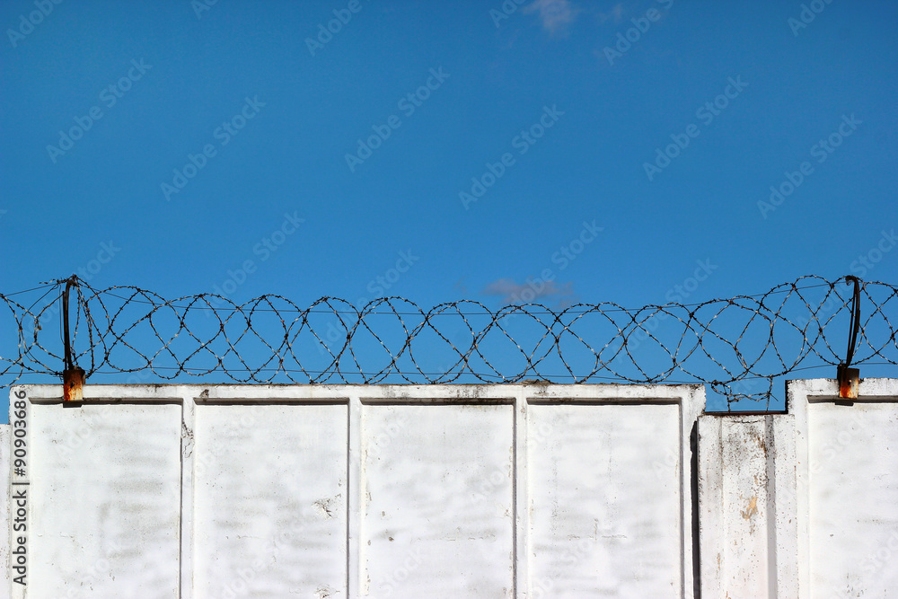 White concrete fence with barbed wire against a blue sky backgro White concrete fence with barbed wire against a blue sky backgro