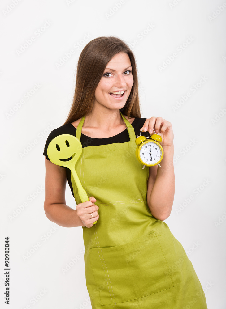 Cheerful girl in yellow apron holding a smiley face spatula and an alarm clock Cheerful girl in yellow apron holding a smiley face spatula and an alarm clock
