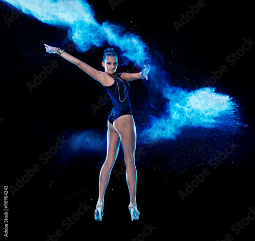 Young woman jumping in blue powder cloud