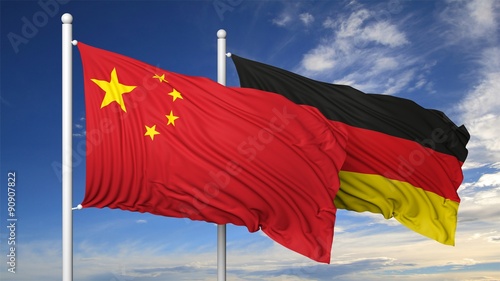 Waving flags of China and Germany on flagpole, on blue sky background. photo