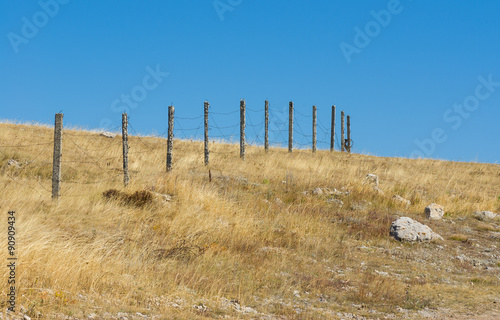 Guarded landscape - barrier with barbed wire against blue cloudless sky
