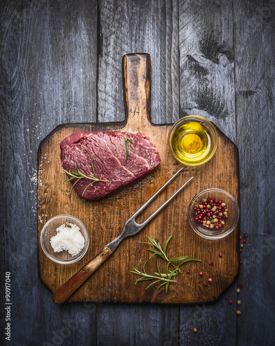 Raw fresh marbled beef steak with meat fork and seasonings  on rustic cutting board over blue wooden background photo
